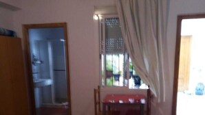 A room with a dining table, chairs, a bed, and a kitchen area visible through an open door. - Alcázar (Córdoba)
