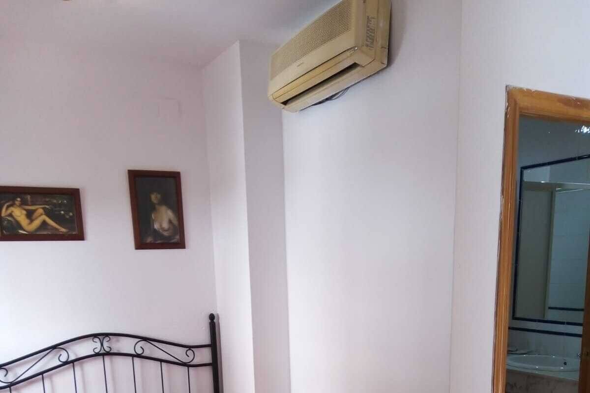 A bedroom with a single bed, a wooden door, and an air conditioning unit on the wall.