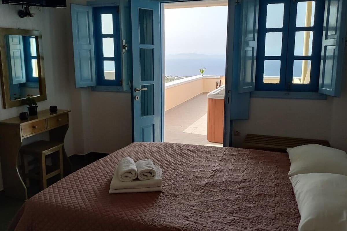 A hotel room with a bed, a desk, a mirror, and a balcony with a view.