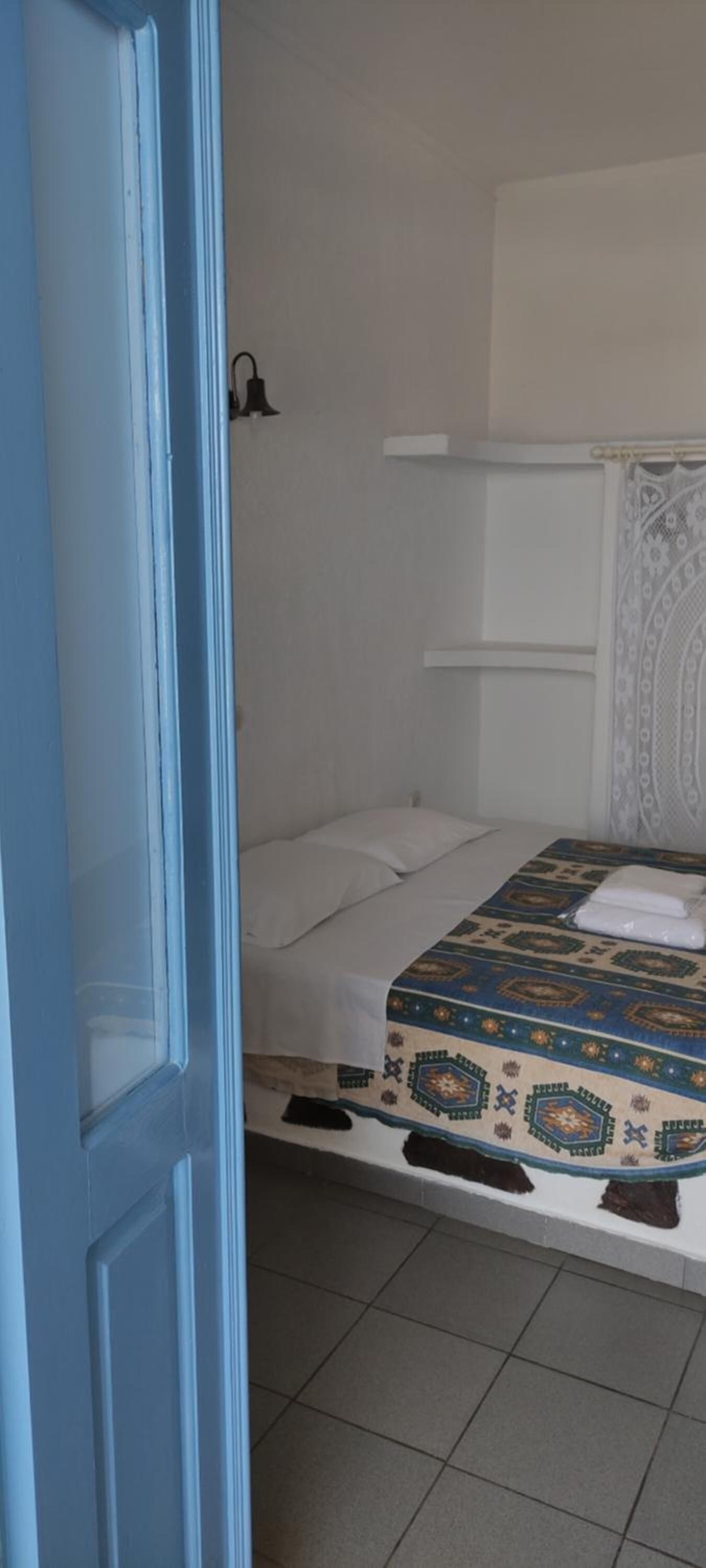 Une chambre avec un lit, une tête de lit blanche, une couvre-lit à motifs et un rideau blanc.