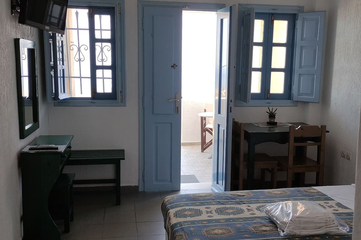 A room with a bed, a desk, a chair, and a table with a potted plant.