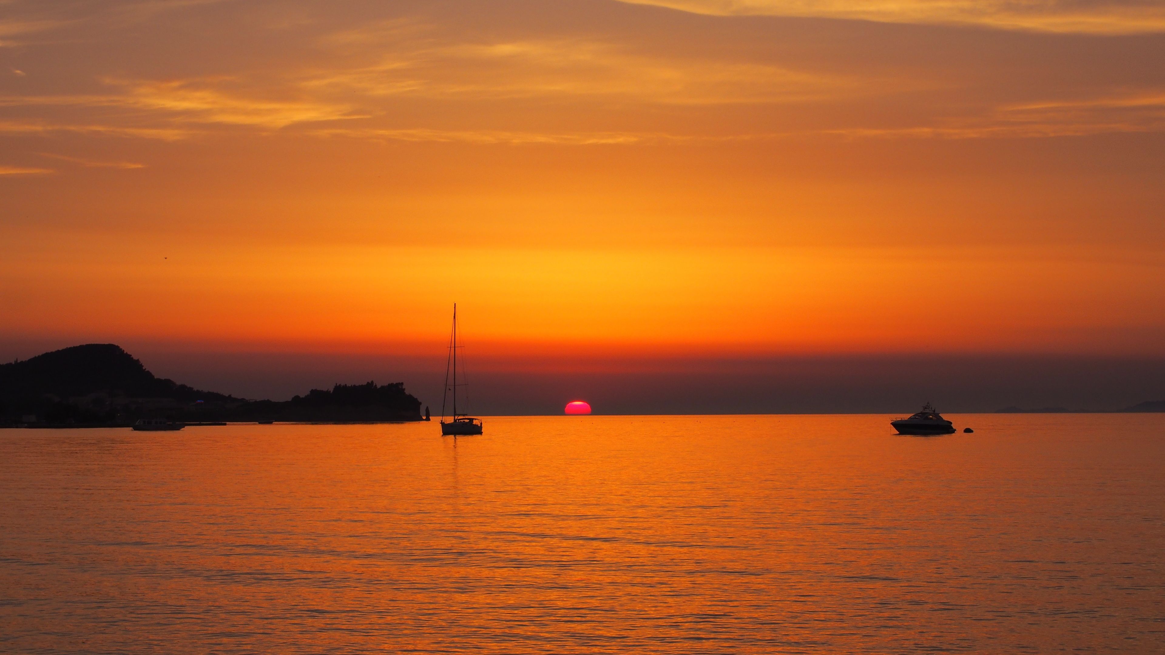 Un atardecer sobre un mar tranquilo con barcos y una tierra distante.