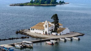 A white church with a bell tower on a small island, surrounded by calm water and boats. - The Wave (Corfu)