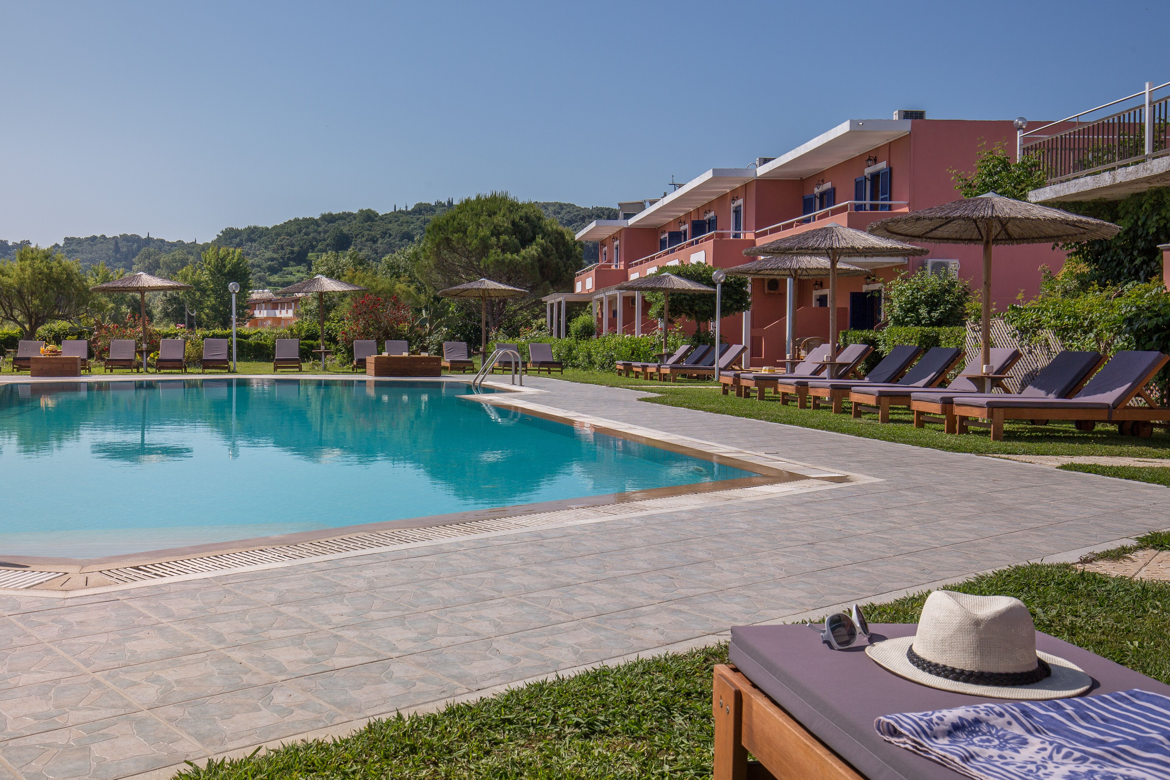 Un área de piscina con sillones y sombrillas, rodeada de edificios con balcones.