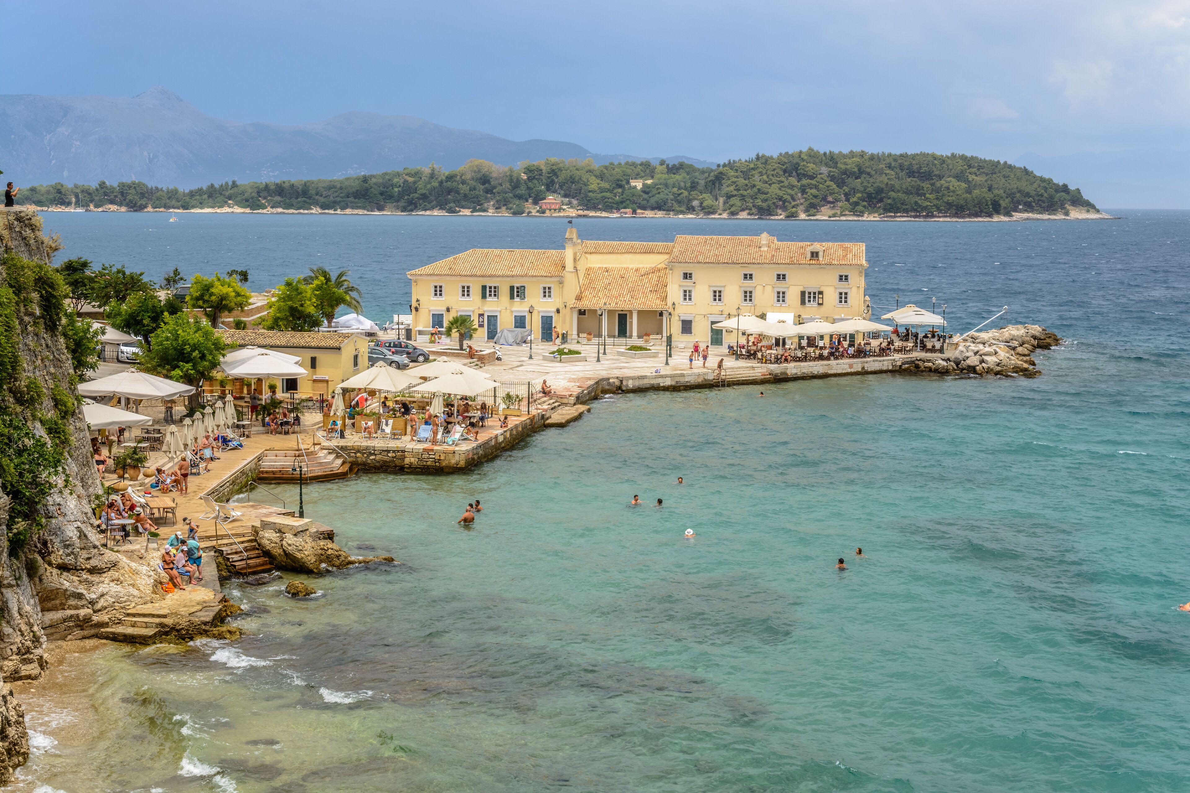A coastal hotel with a pool area, outdoor seating, and a view of the sea.