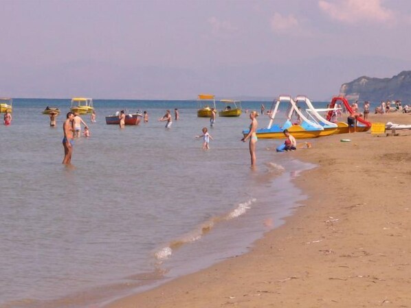 A beach with people swimming and playing, boats, and a water slide.