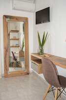 Una habitación con escritorio de madera, una silla, un espejo, un televisor y una planta.