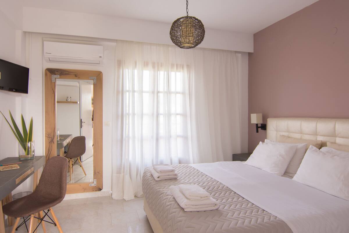 A hotel room with a bed, a desk, a chair, a TV, and a window with curtains.
