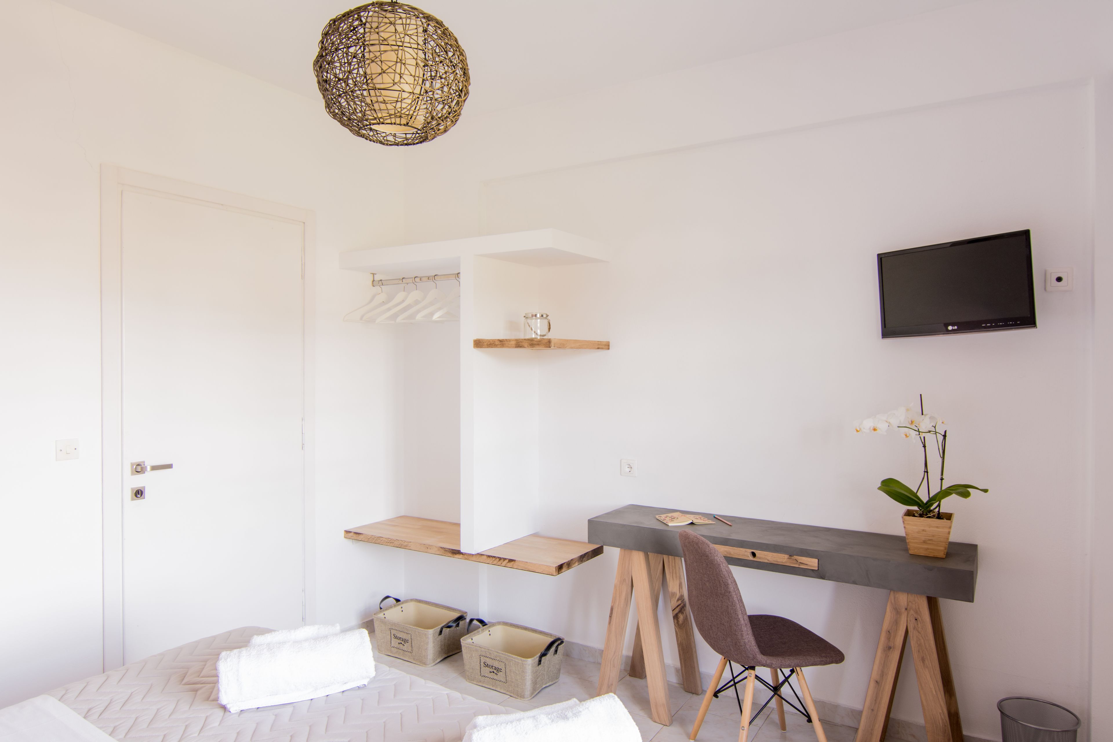 A modern, minimalist room with a bed, a desk, a chair, a television, and a hanging light fixture.