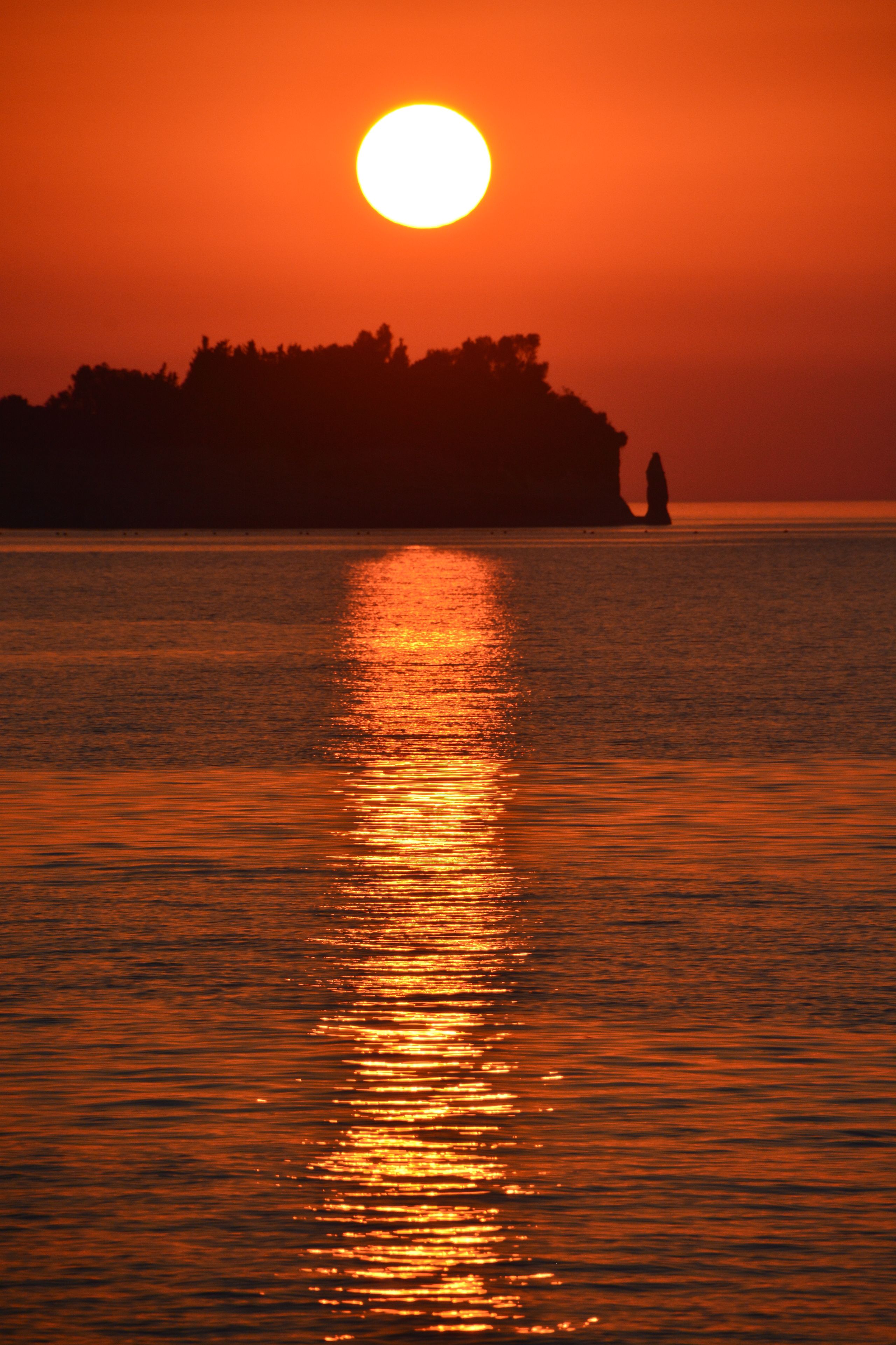 Un atardecer sobre aguas tranquilas, con la silueta de una masa de tierra y una sola figura de pie sobre ella.