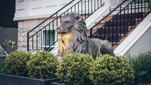 Une statue de lion en pierre se trouve devant une maison avec un escalier.