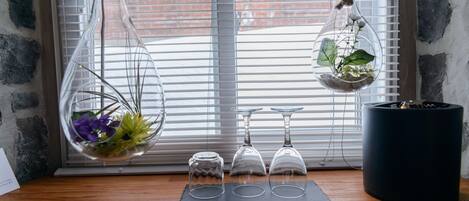 A wooden shelf with three glass terrariums, a potted plant, and two wine glasses.