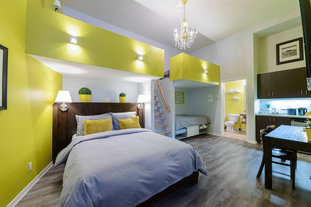 A bedroom with a bed, bedside lamps, a chandelier, and a small plant.