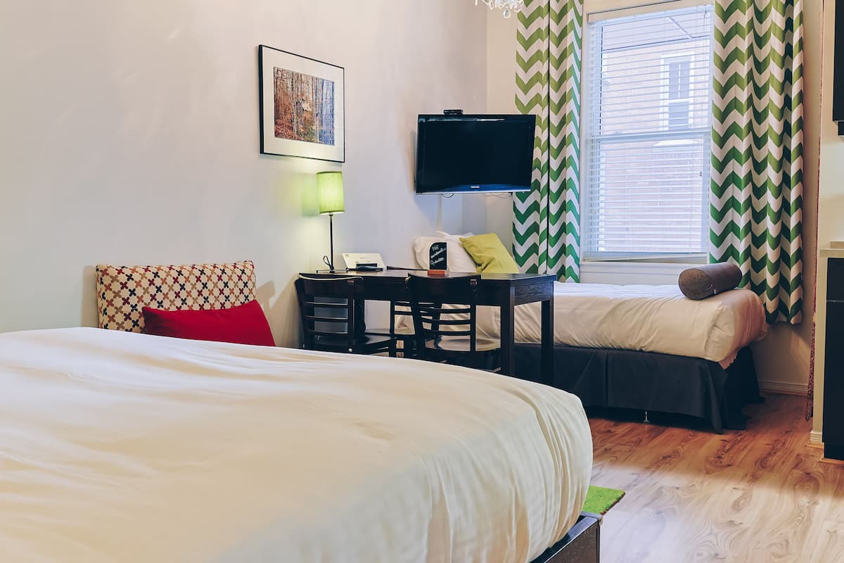A hotel room with a large bed, a desk with a chair, a television, and a window with curtains.