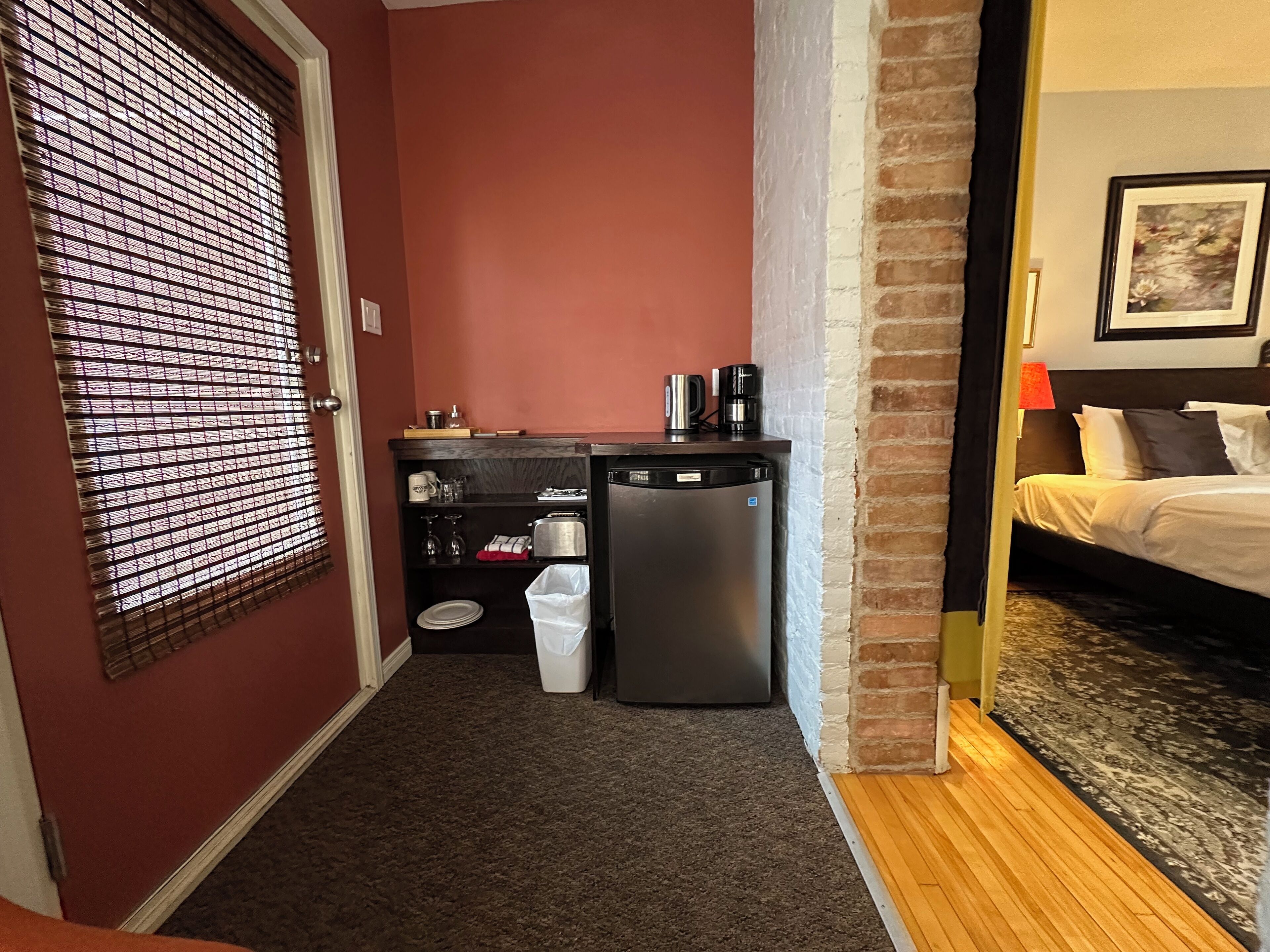 Quarto de hotel pequeno com cozinha compacta, um cesto de lixo e uma cama com cabeceira.