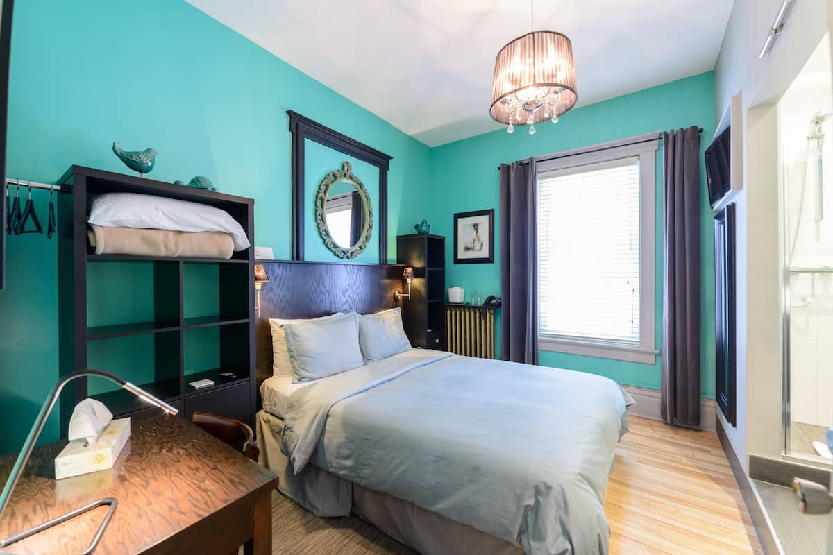 A bedroom with a bed, a desk, a dresser, a mirror, and a window with curtains.