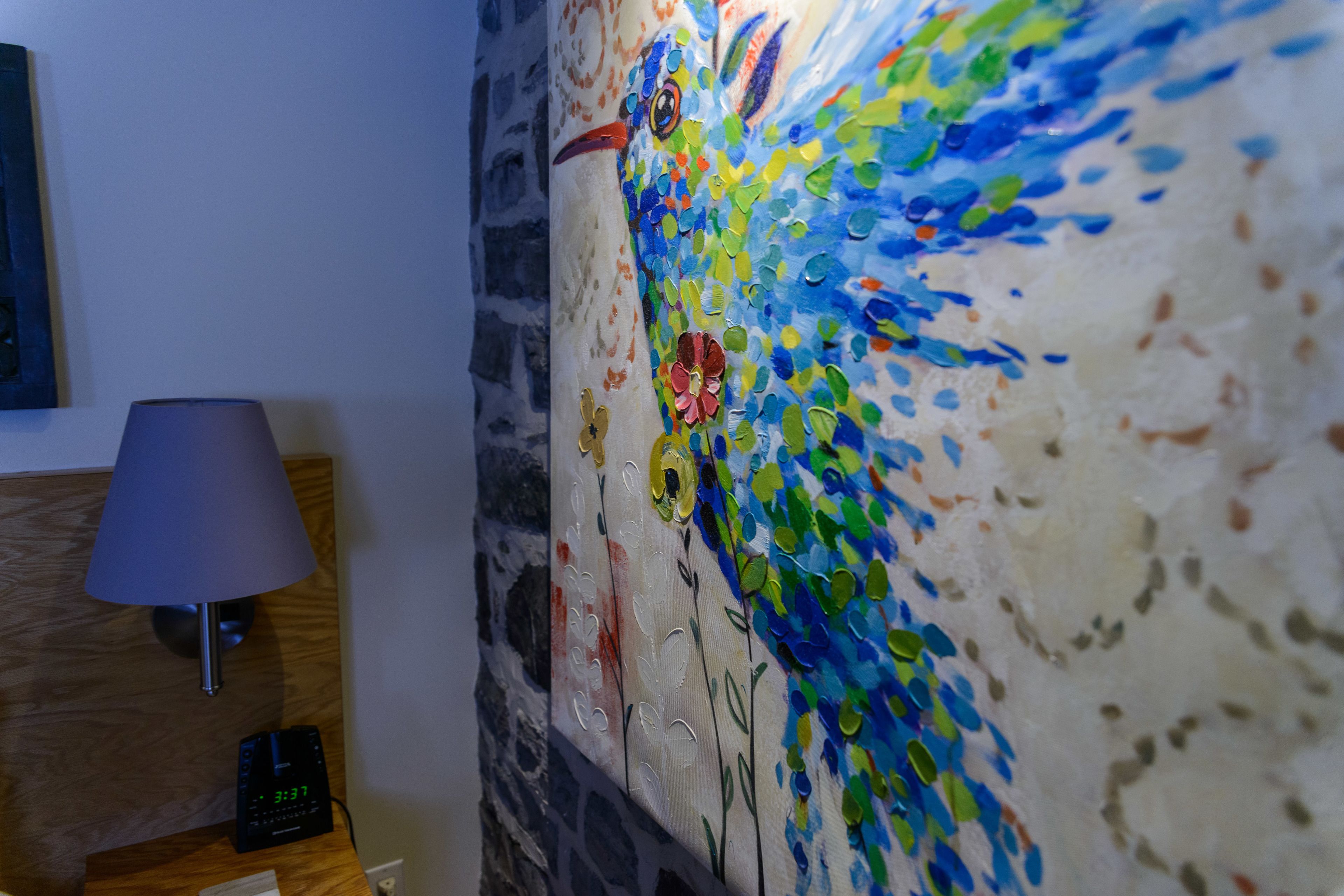 Una pared con un mosaico artístico y una lámpara sobre una mesita de noche de madera.