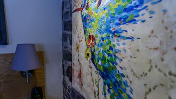 Una pared con un mosaico artístico y una lámpara sobre una mesita de noche de madera.
