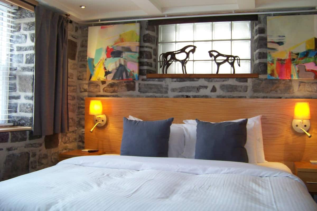 A hotel room with a large bed, stone wall, and artwork above the bed.