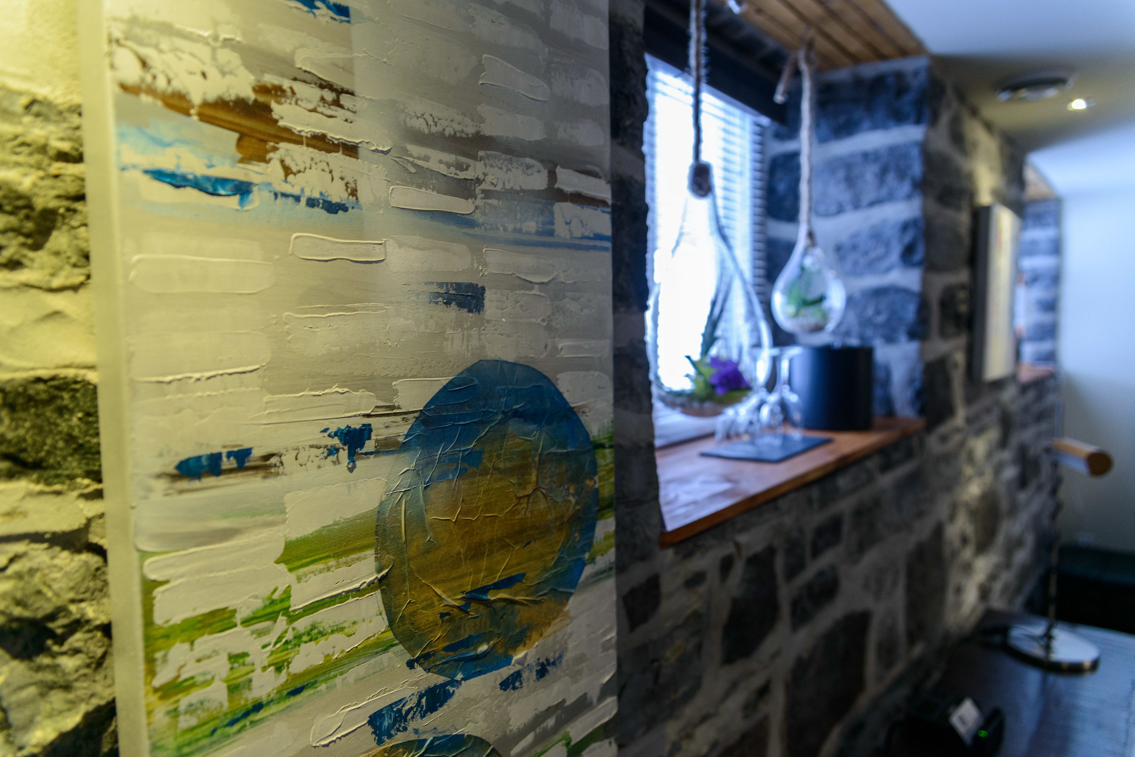 A rustic stone wall with a wooden shelf holding a blue pot and a hanging light fixture.