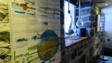 A rustic stone wall with a wooden shelf holding a blue pot and a hanging light fixture.