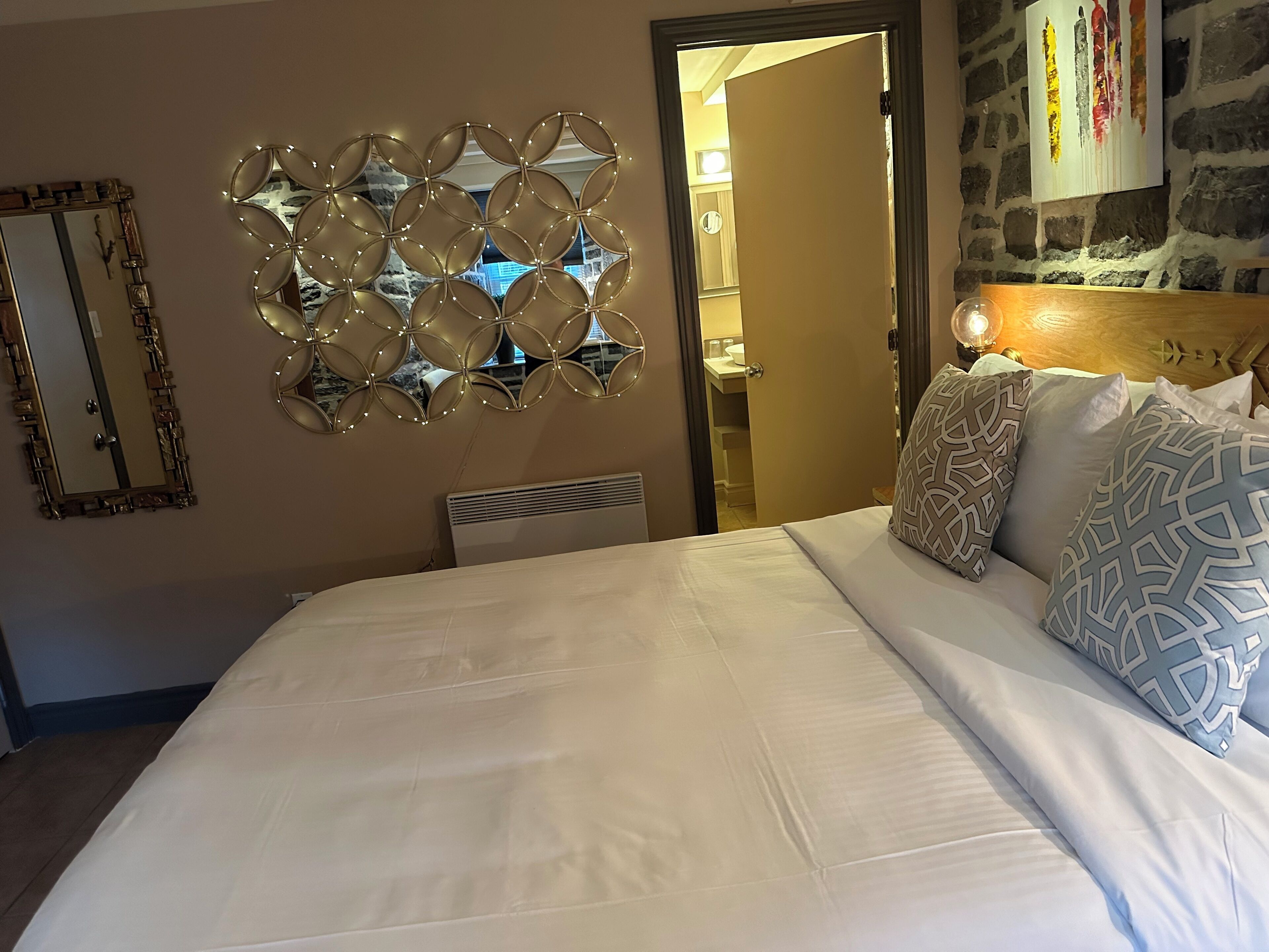 Une chambre d’hôtel avec un grand lit, des miroirs décoratifs sur les murs et une vue sur la salle de bain par une porte ouverte.