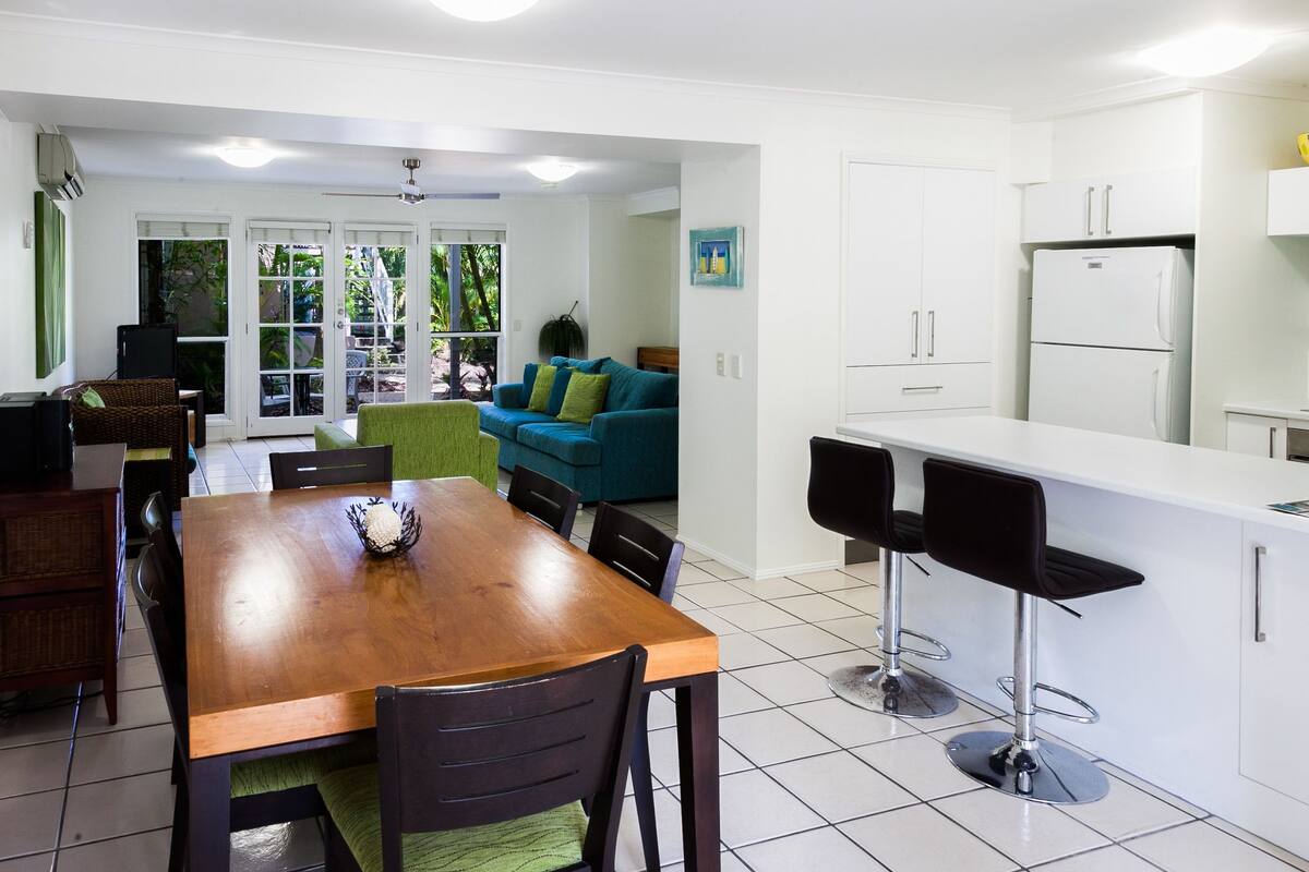 Una cocina moderna con armarios blancos, una mesa de comedor de madera y taburetes negros.