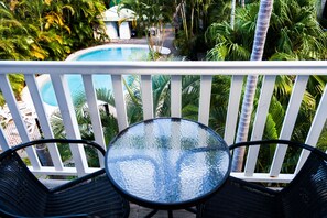 Un balcón con mesa y sillas de vidrio que da a una piscina rodeada de exuberante vegetación.