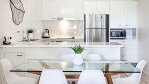 Una cocina moderna con gabinetes blancos, electrodomésticos de acero inoxidable y una mesa de comedor de vidrio con sillas blancas.