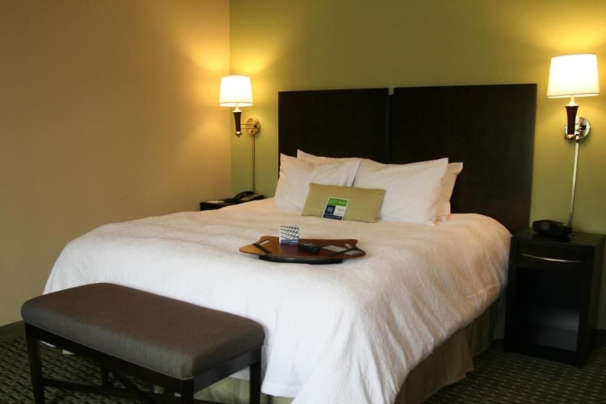 A hotel room with a large bed, bedside lamps, a bedside phone, a tray with a remote control, and a bench.