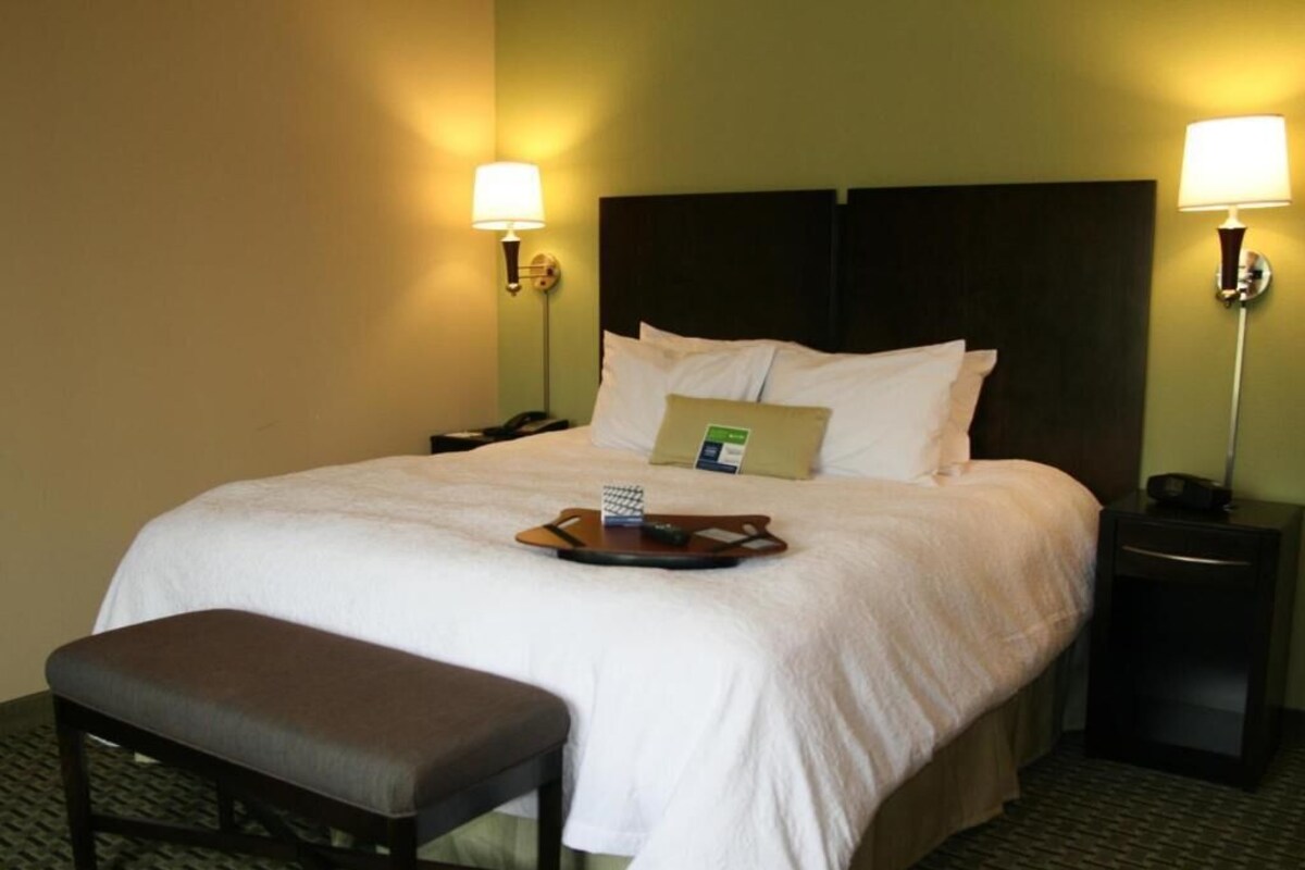 A hotel room with a large bed, bedside lamps, a bedside phone, a tray with a remote control, and a bench.