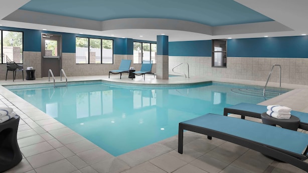 Una piscina interior moderna con agua azul cristalina, sillones de descanso y suelo de baldosas.