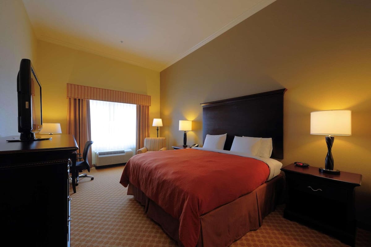 A hotel room with a large bed, two bedside tables with lamps, a desk with a computer, and a chair.