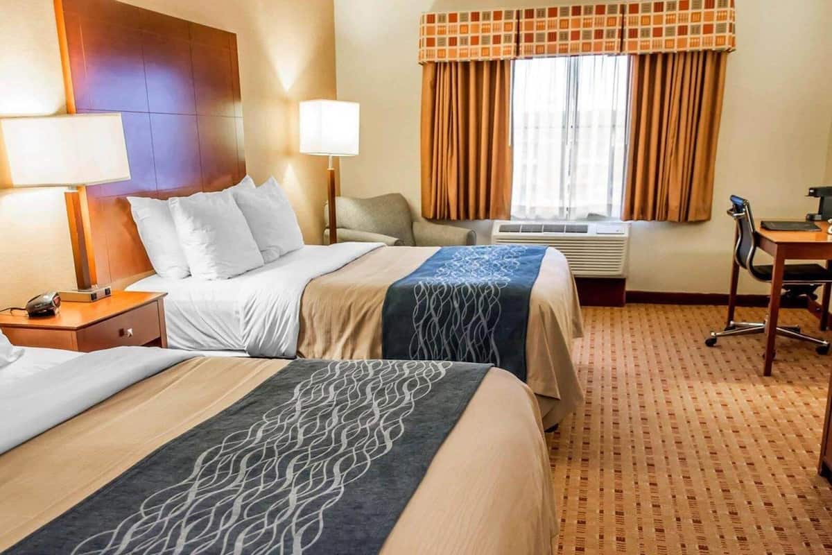 Une chambre d’hôtel avec deux lits, un bureau, une chaise, une lampe et un appareil de climatisation.