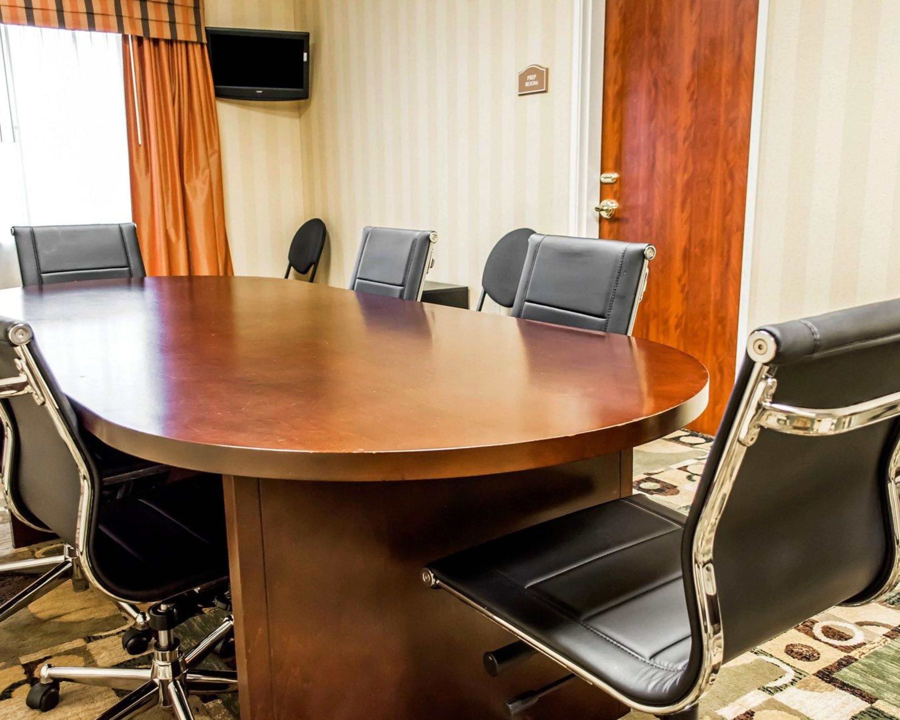 A conference room with a large oval table, six black leather chairs, and a television on the wall.
