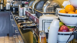 Un buffet proposant une variété de plats et de boissons, notamment des fruits et un distributeur de jus.