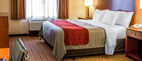 Habitación de hotel con cama, escritorio, silla, lámpara y ventana con cortinas.