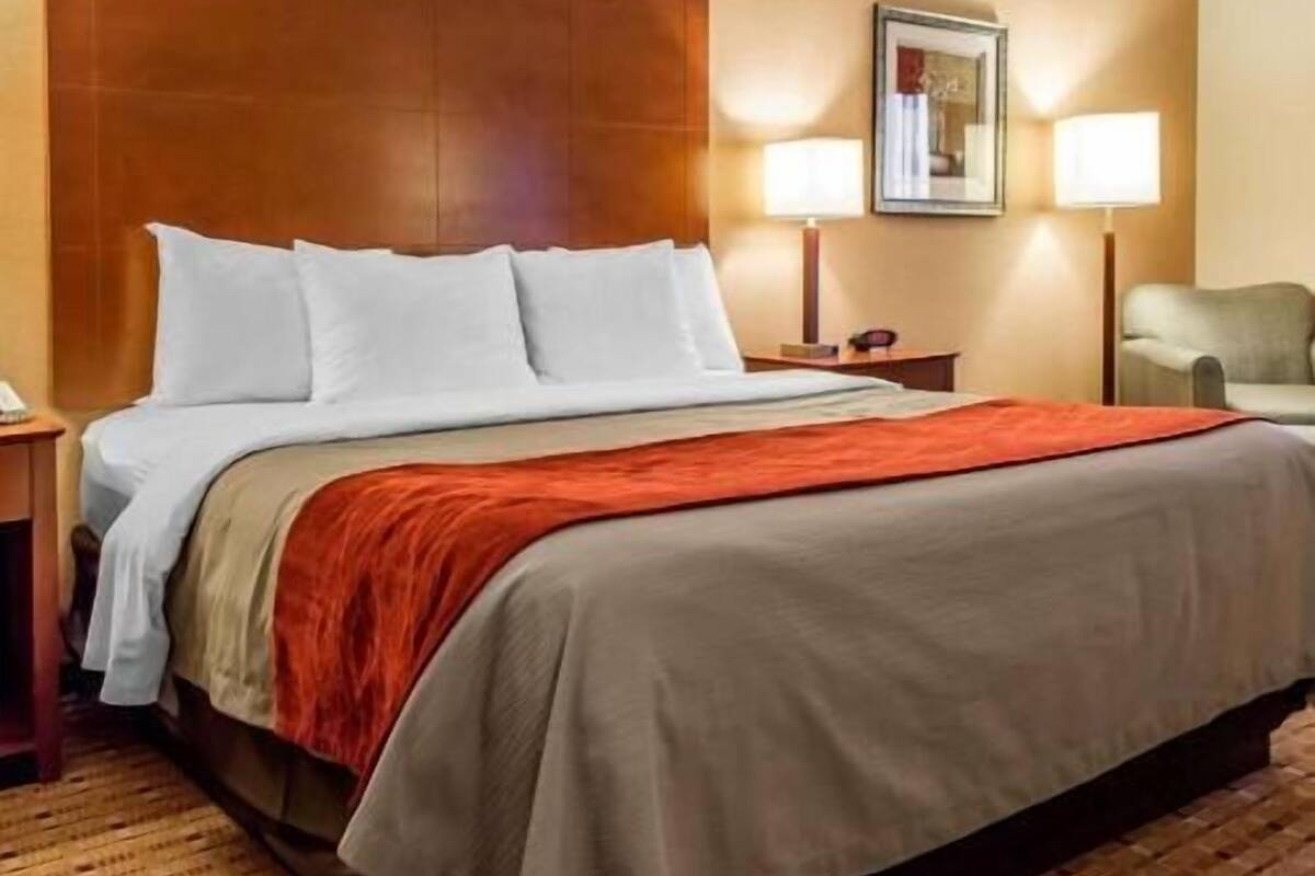 Une chambre d’hôtel avec un grand lit, une tête de lit en bois, une table de chevet, une lampe et une chaise.