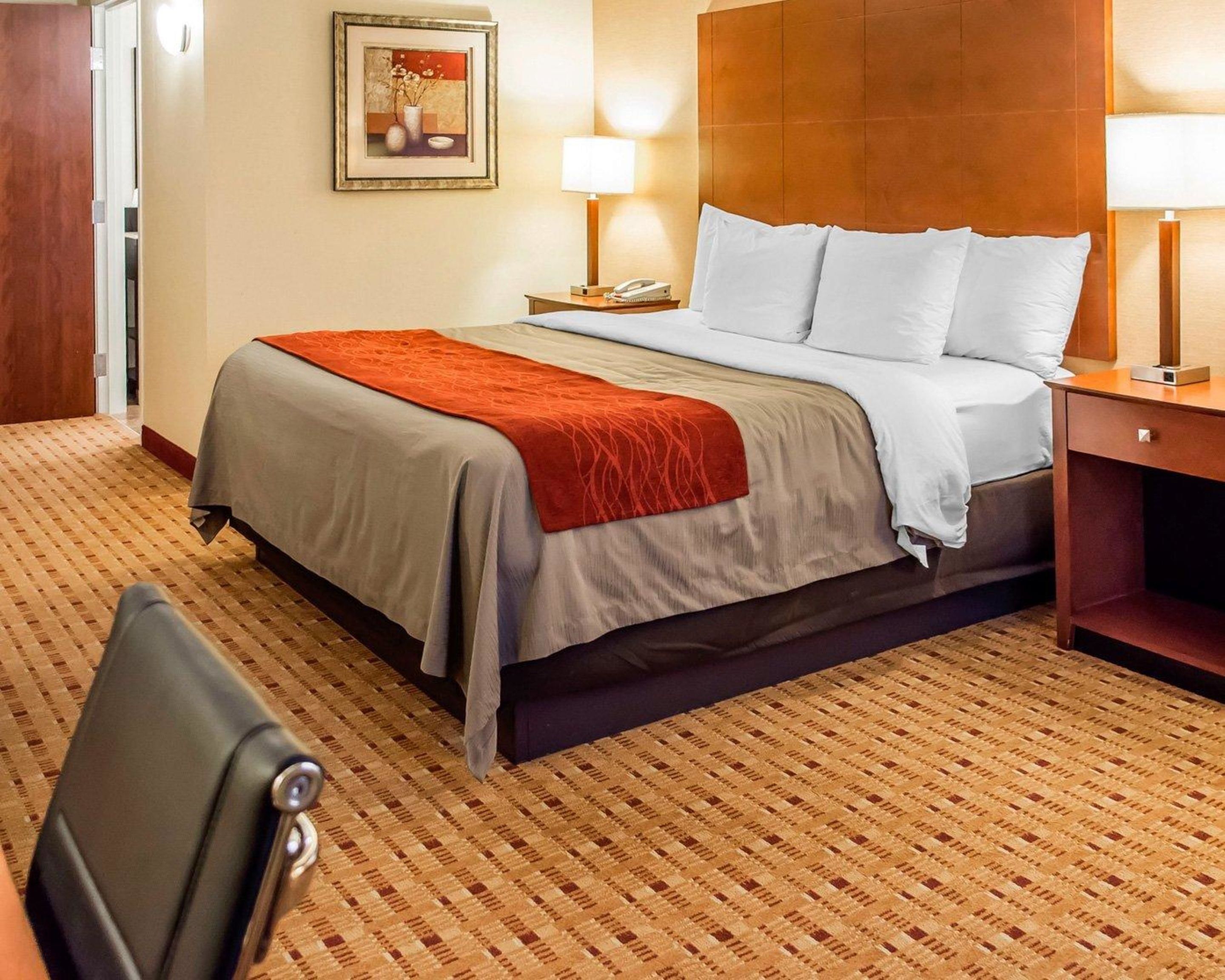 A hotel room with a bed, two bedside lamps, a nightstand, a framed picture on the wall, and a chair.