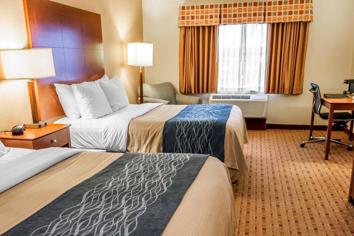 Une chambre d’hôtel avec deux lits, un bureau, une chaise et une fenêtre avec des rideaux.