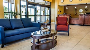 Un hall d’entrée avec un canapé bleu, un fauteuil rouge, une table basse en verre et un comptoir d’accueil.