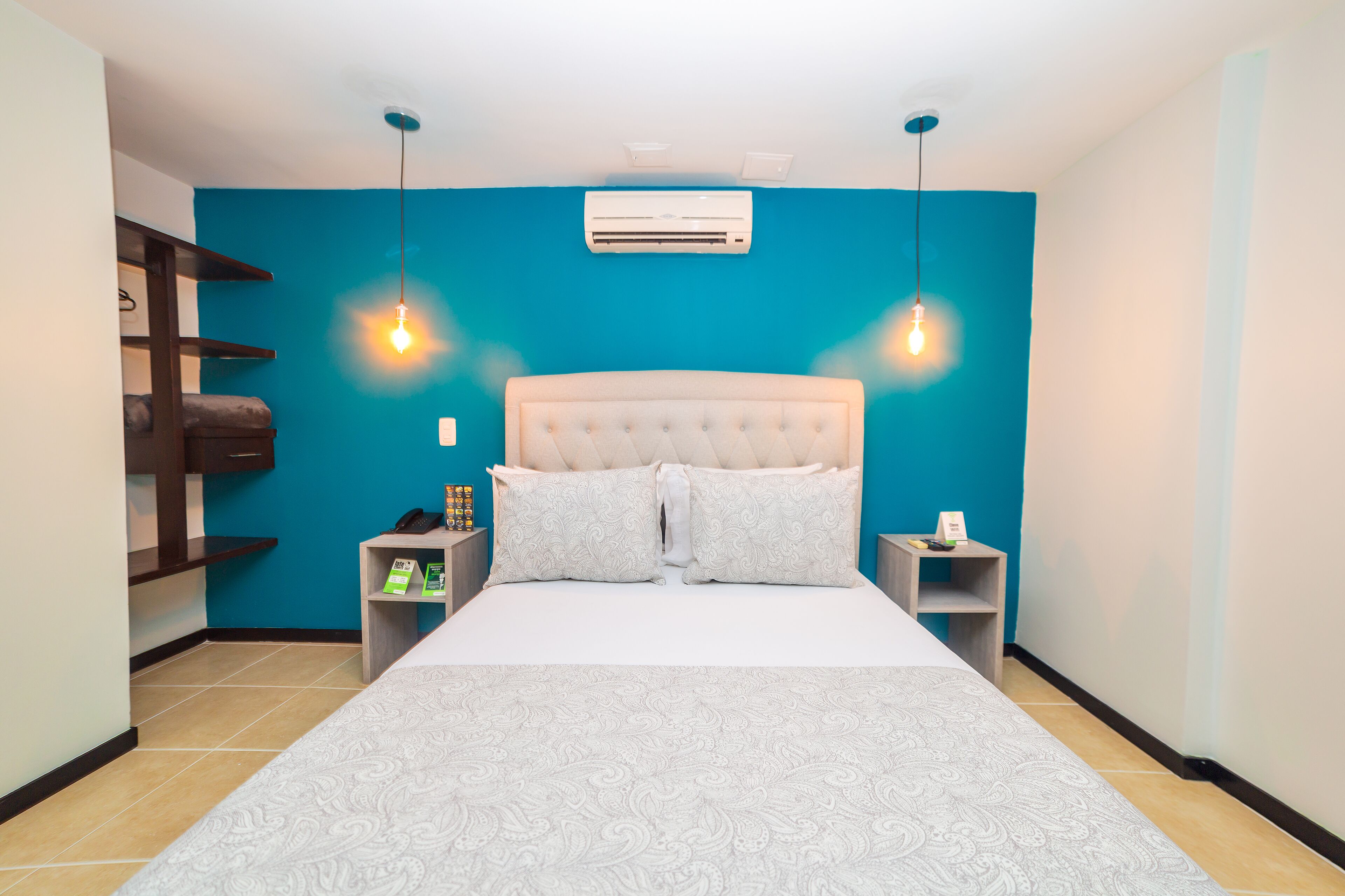 Une chambre avec un grand lit, deux tables de chevet, une commode, un climatiseur mural et un mur d’accent bleu.