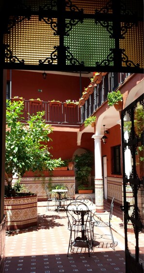 An outdoor patio with a table and chairs, surrounded by potted plants and a decorative railing.