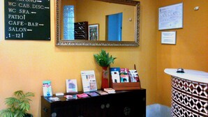 A reception area with a mirror, a signboard with directions, a potted plant, a counter with magazines, and a patterned cabinet. - Hotel Al Andalus Jerez (Jerez de la Frontera)