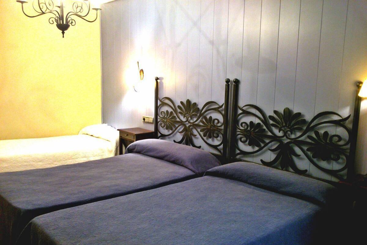 Una habitación con dos camas, una lámpara de pared y una mesita de noche con lámpara.