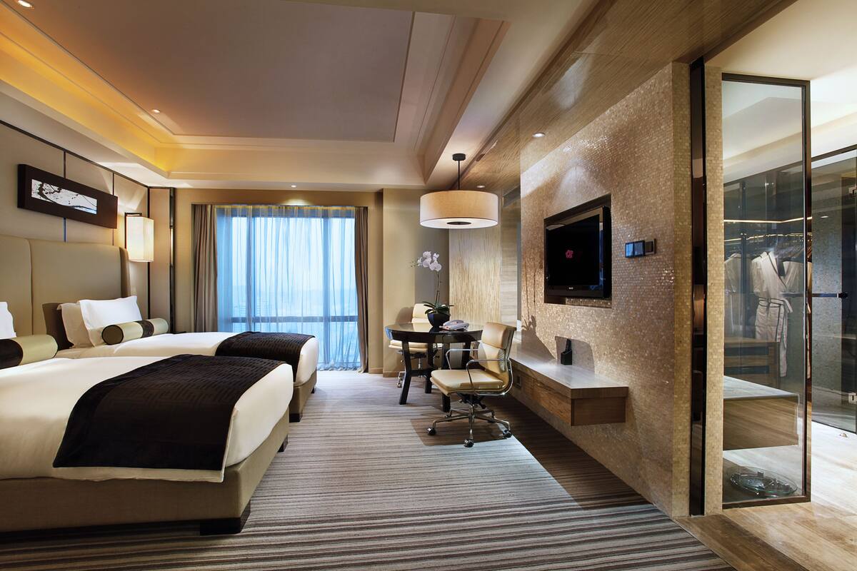 Une chambre d’hôtel avec un grand lit, un bureau, une chaise, une télévision et un placard fermé par des portes en verre.