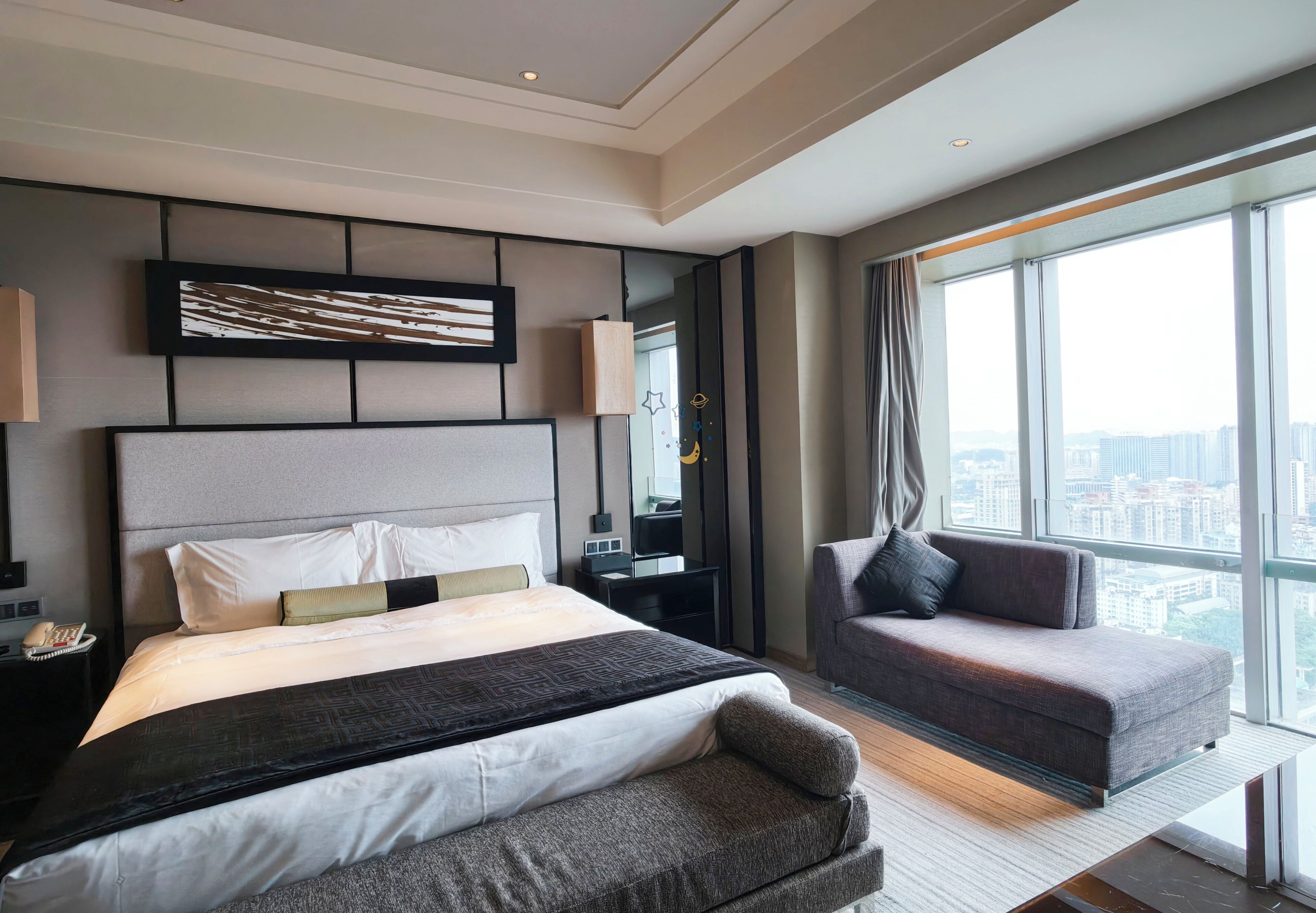 Quarto de hotel moderno com uma cama grande, um sofá, uma escrivaninha e vista para a cidade.