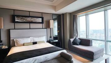 Quarto de hotel moderno com uma cama grande, um sofá, uma escrivaninha e vista para a cidade.