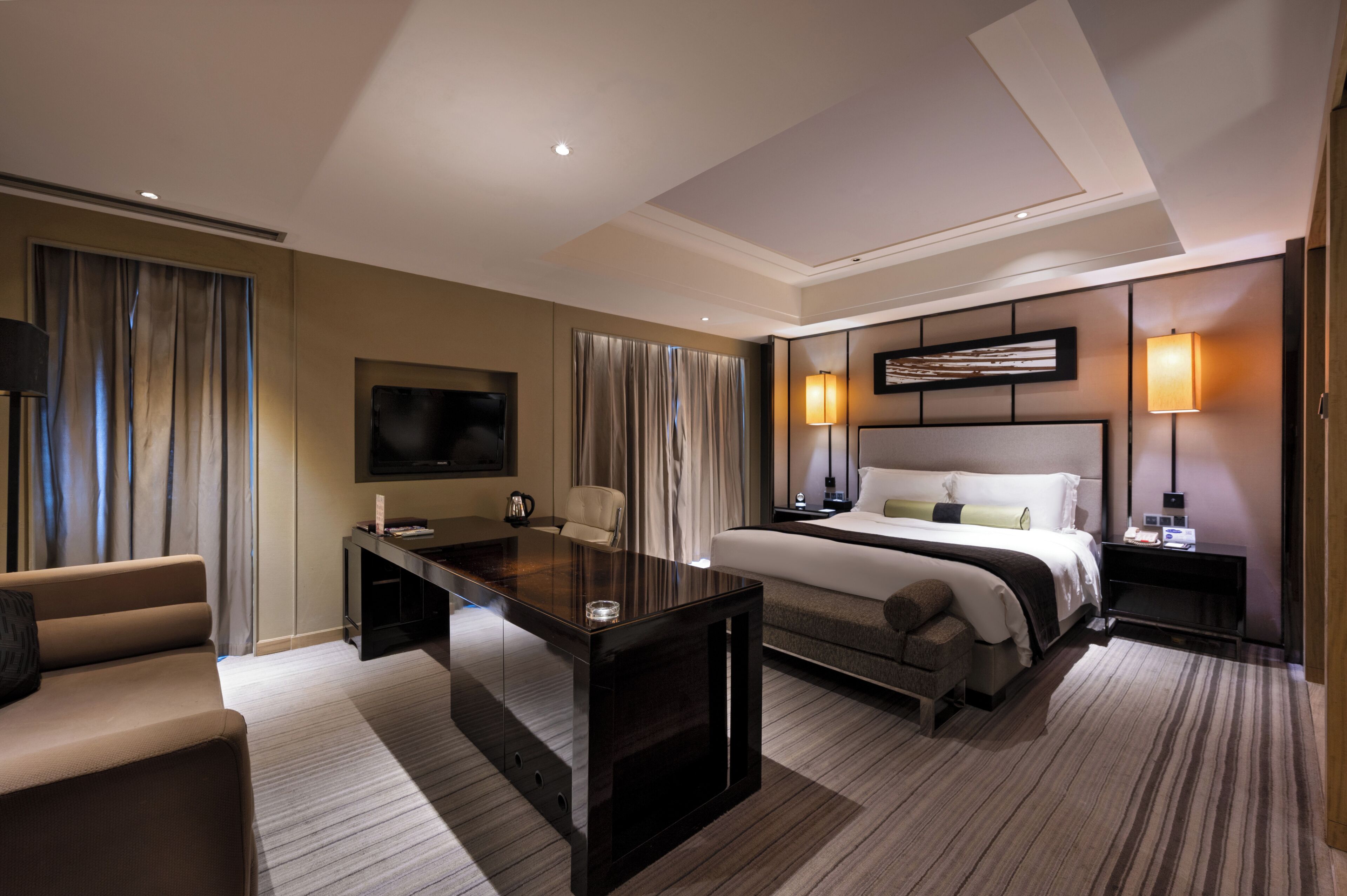 A hotel room with a bed, a desk, a chair, a TV, and a bedside table.