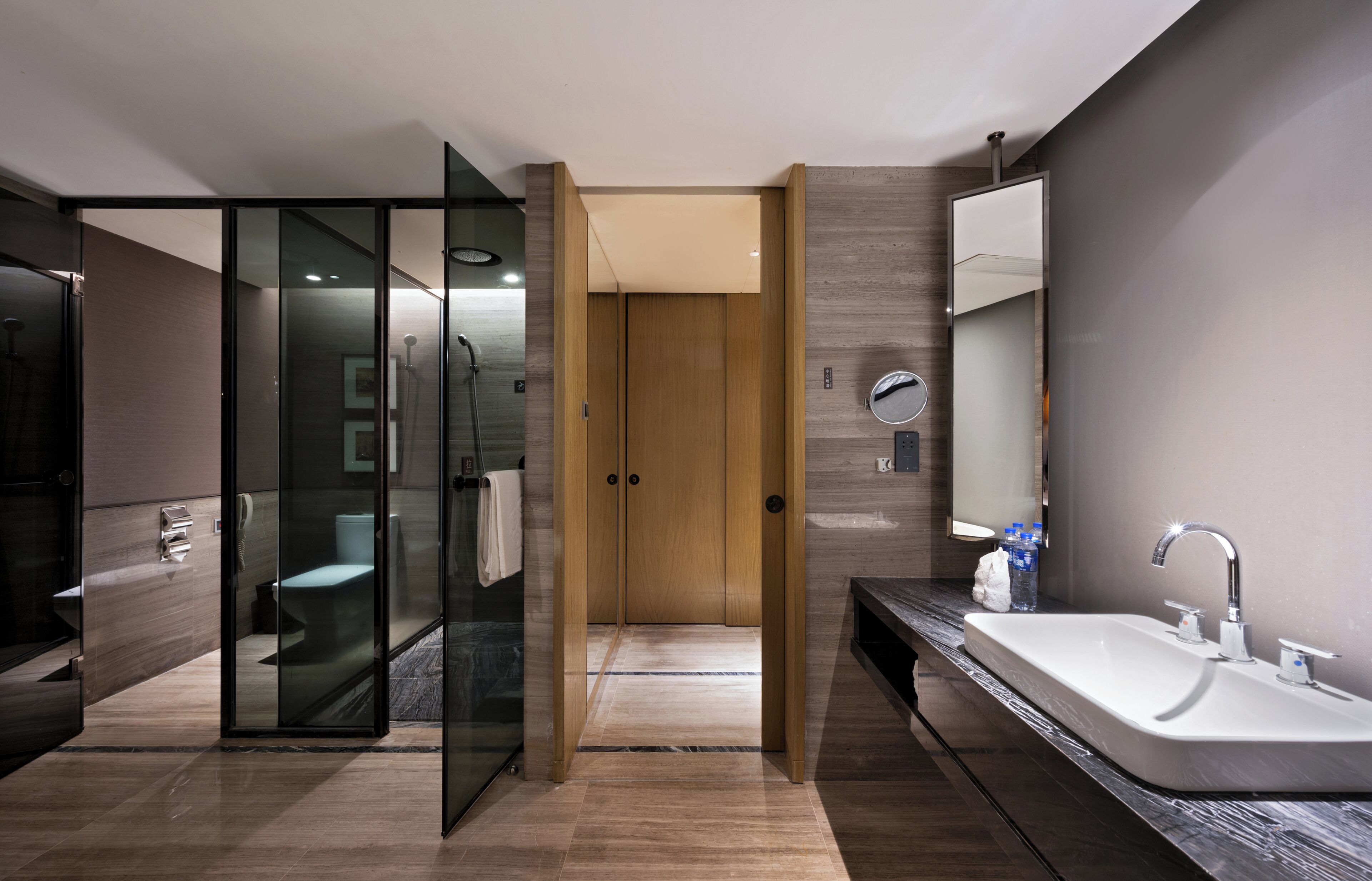 Un baño moderno con ducha envuelta en vidrio, puerta de madera y tocador con lavamanos y espejo.